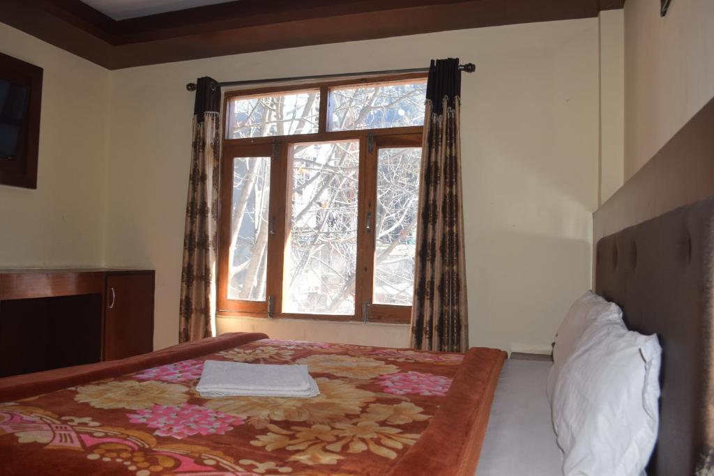 a bedroom with a bed with a large window at Hotel Tridev Manali in Manāli