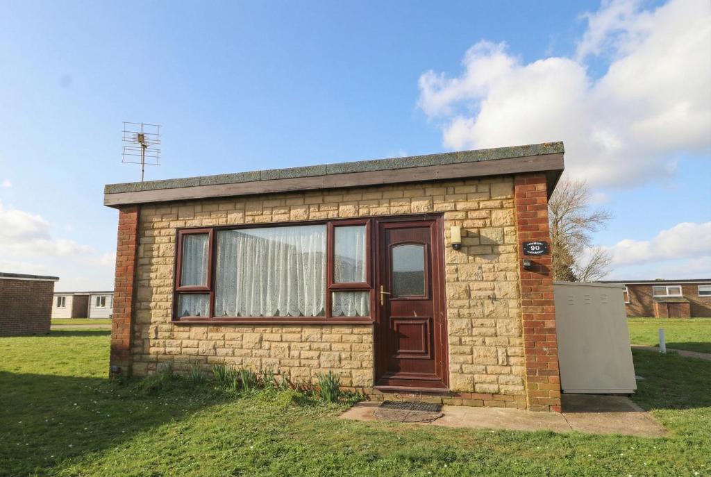 a small brick house with a door in the grass at 90 Bay View in New Romney