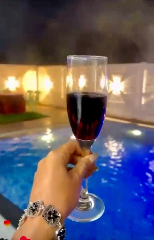 a person holding a glass of wine next to a pool at Amigos Farm in Lucknow