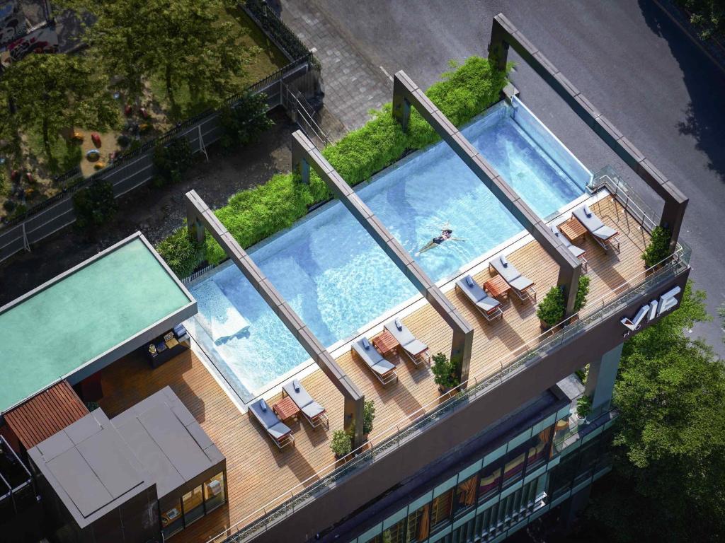 A second aerial view looks down on the rooftop pools, loungers, greenery, and surrounding city streets.