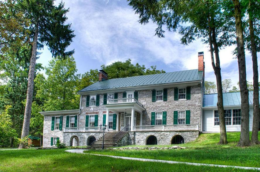 a large stone house with a porch and trees at Stocks Manor Bed and Breakfast in Mechanicsburg