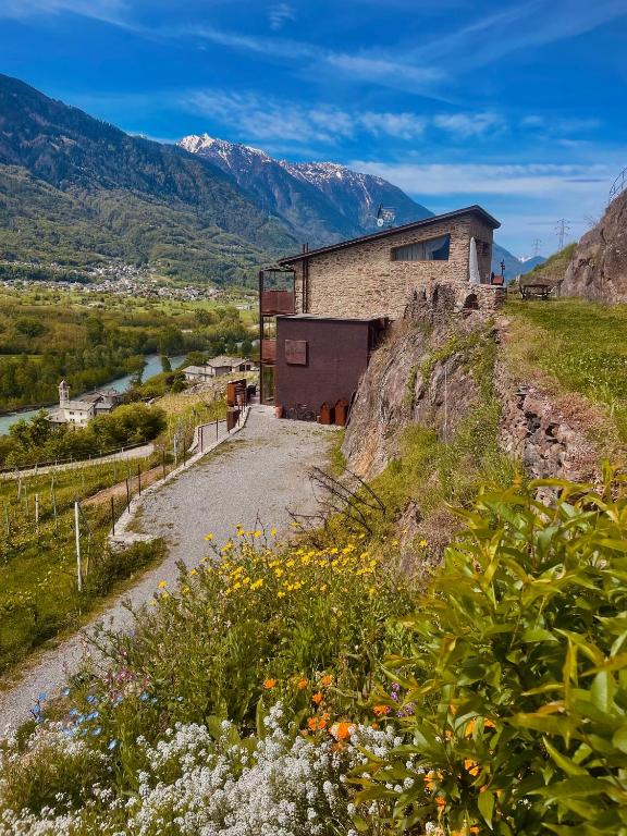 a building on a hill with a river and mountains at Ca' Barroni - Vineyard Escape in Sondrio