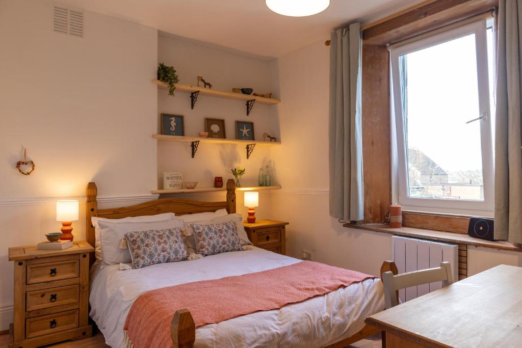 a bedroom with a bed and a table and a window at Hallbank Hideout in Amble