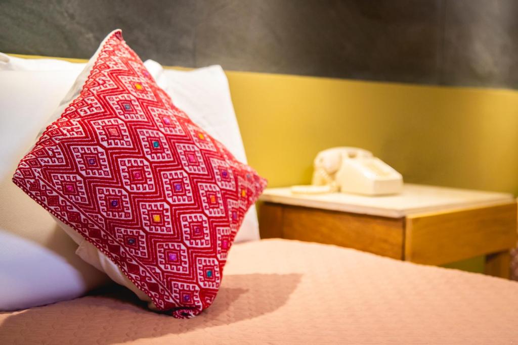 a red pillow sitting on a bed next to a telephone at Hotel Uniko in San Cristóbal de Las Casas