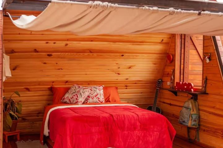 a bedroom with a red bed with a wooden wall at Glampiri in Pirenópolis