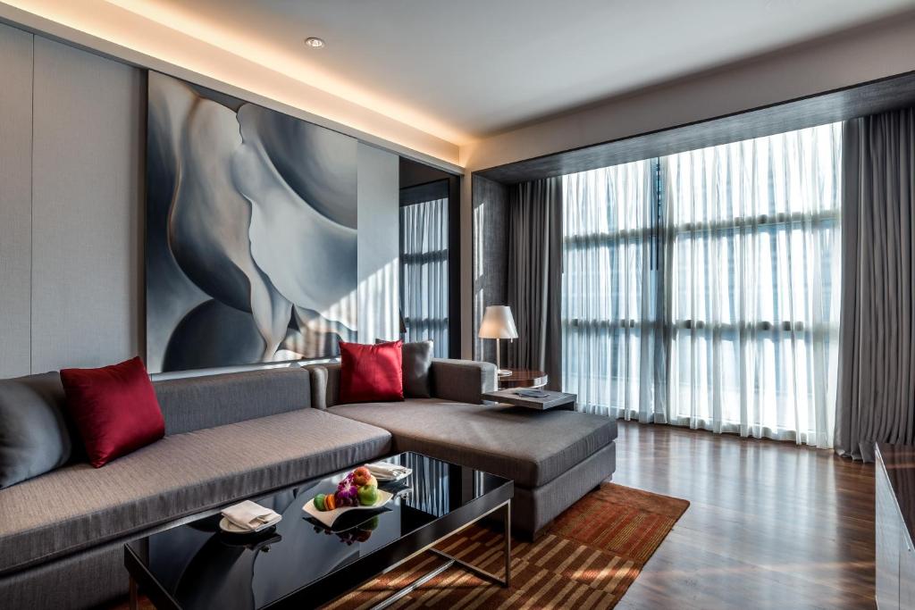 A bright suite lounge with an L-shaped sofa, coffee table, and full-height window.