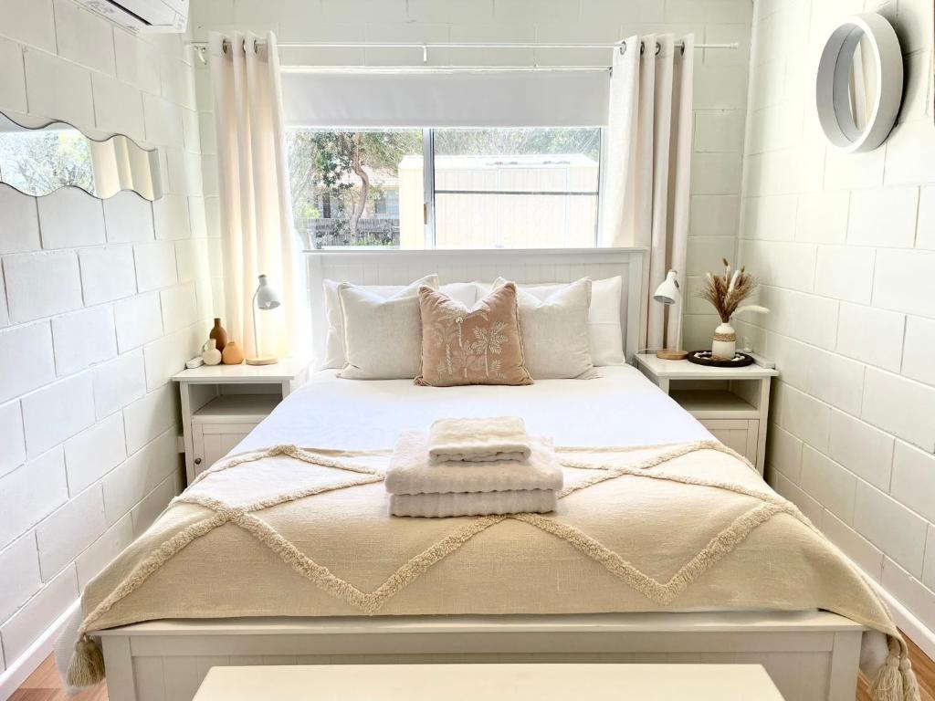 a white bedroom with a bed with a window at Family & Couples Beachside Stay Ocean Glimpses 7 day Xmas 2026 available in Brooms Head