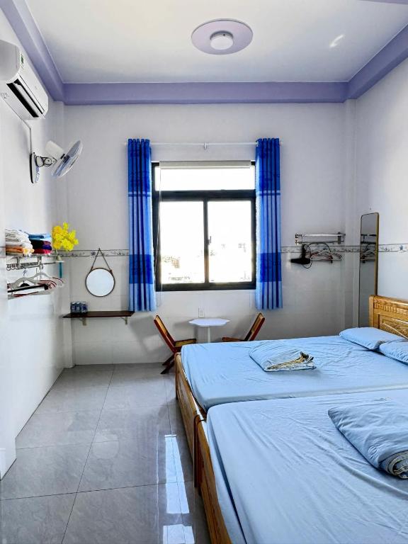 a bedroom with two beds and a window with blue curtains at Homestay Hoàng Phúc in Cu Lao Thu