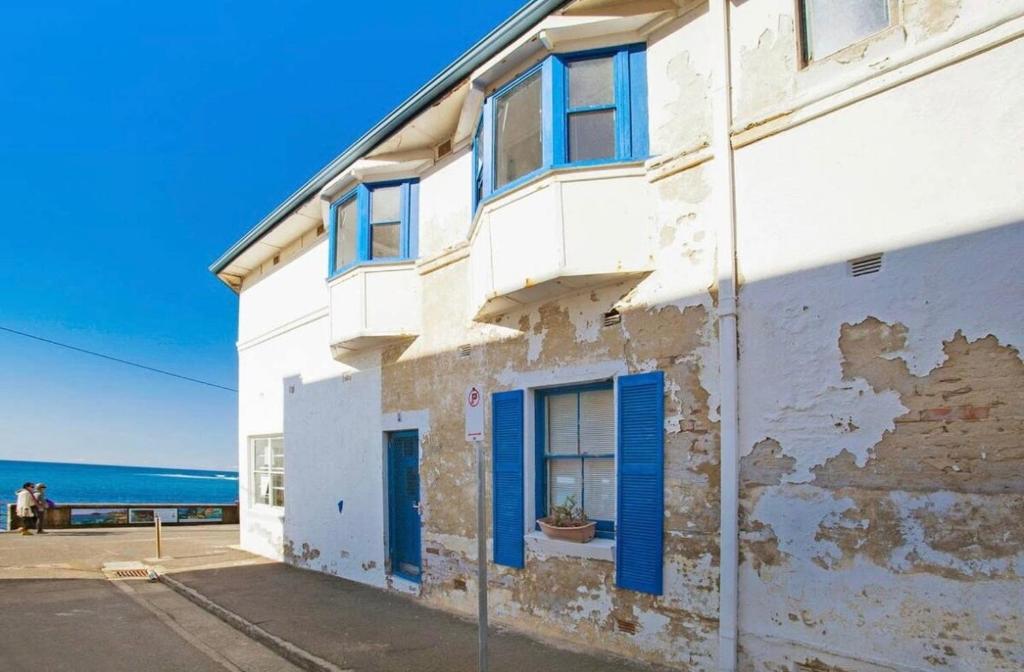 a white building with blue windows and the ocean at Manly Beach Studio in Sydney