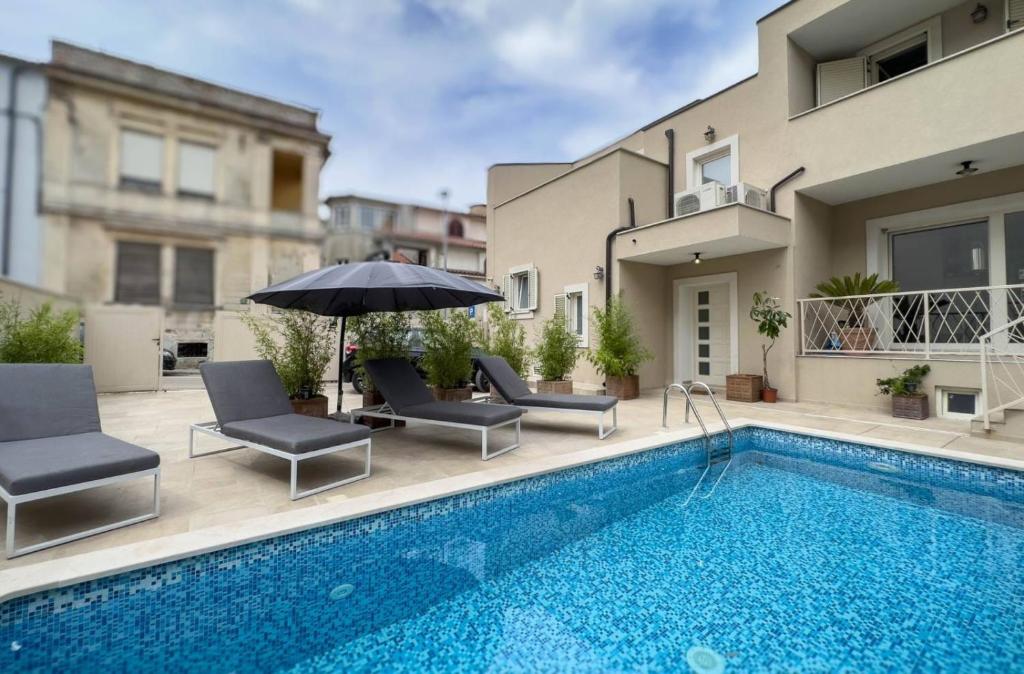 a swimming pool with chairs and an umbrella next to a building at Villa Damiani " Partys and loud music forbidden!!!" in Pula