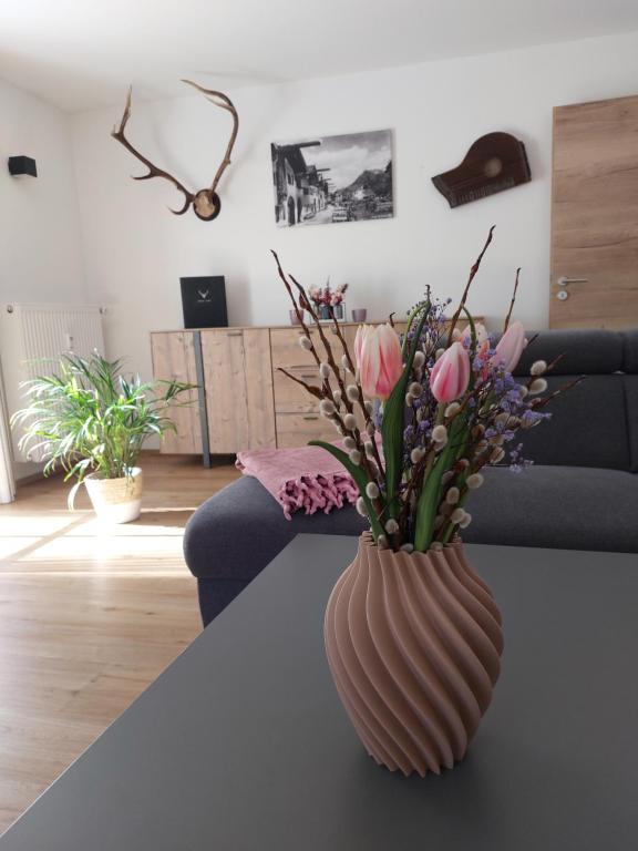 a vase with flowers on a table in a living room at Haus Kurparkblick Ferienwohnung Lautersee in Mittenwald