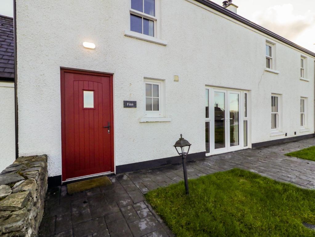 a white house with a red door and a yard at Finn Cottage in Strabane