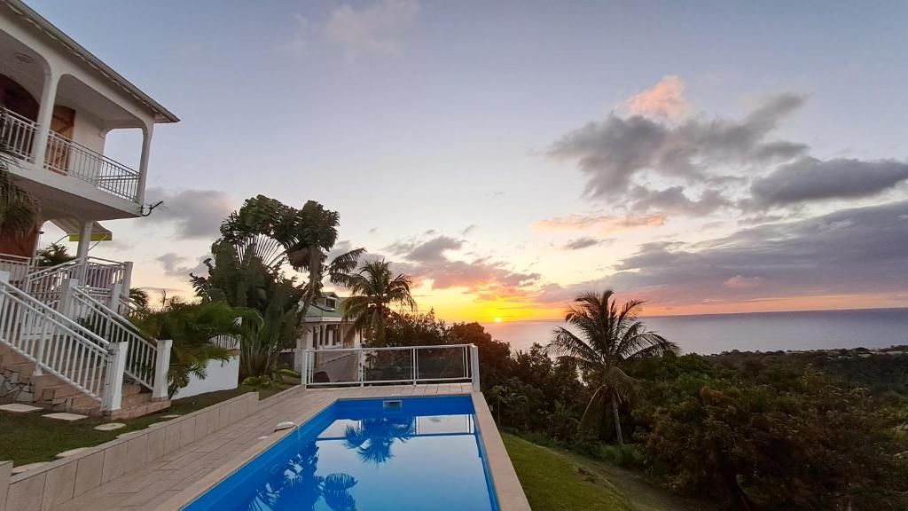 a house with a swimming pool in front of a sunset at Gîte des voyageurs in Vieux-Habitants