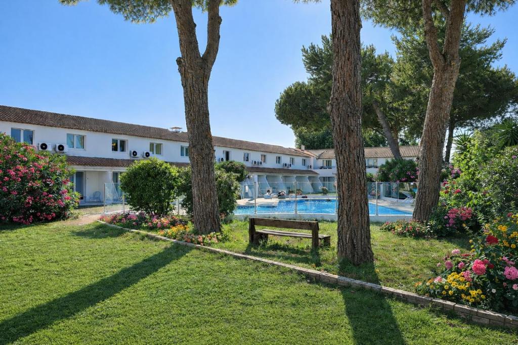 a resort with a swimming pool and trees and a bench at Artemia Aigues-Mortes - Hôtel avec piscine - Bornes électriques - Parking privé - Local vélo-moto in Aigues-Mortes