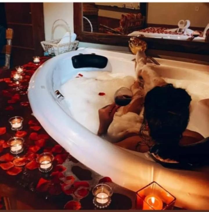 a bathtub filled with candles and roses in a bathroom at Chalés românticos com hidromassagem e lareira em área rural de visconde de Mauá Pousada Bela Helena in Visconde De Maua