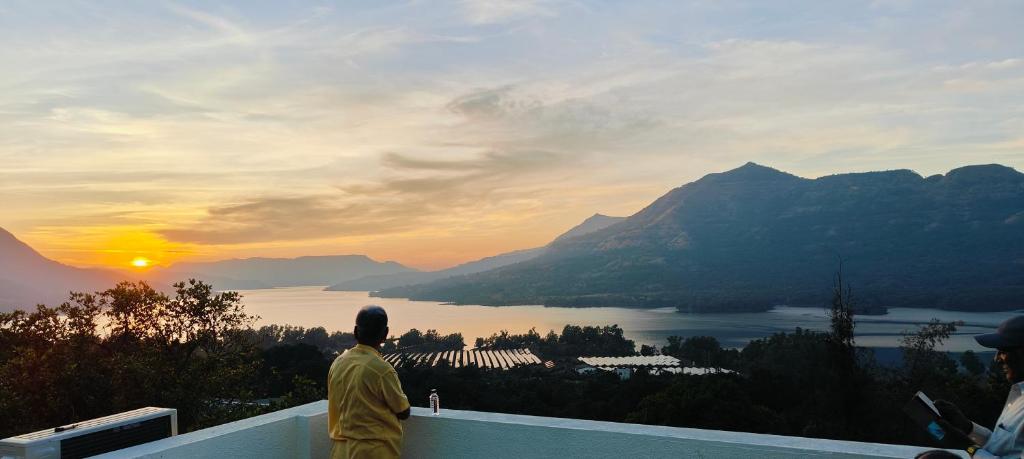 a man standing on a ledge looking at the sunset at Yatri Lakeview Villa in Pune
