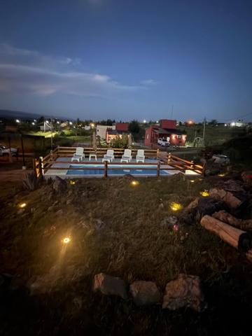a yard with chairs and a pool at night at L&M Cabañas Villa Yacanto in Villa Yacanto