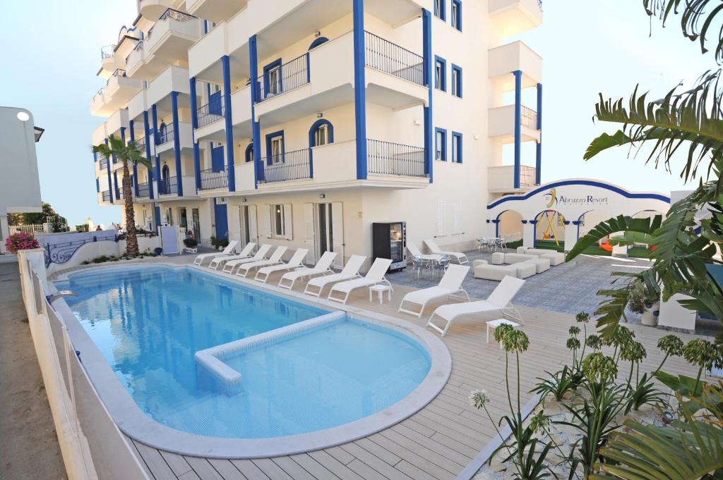 una piscina frente a un edificio con sillas y un hotel en Residence Abruzzo Resort en Tortoreto