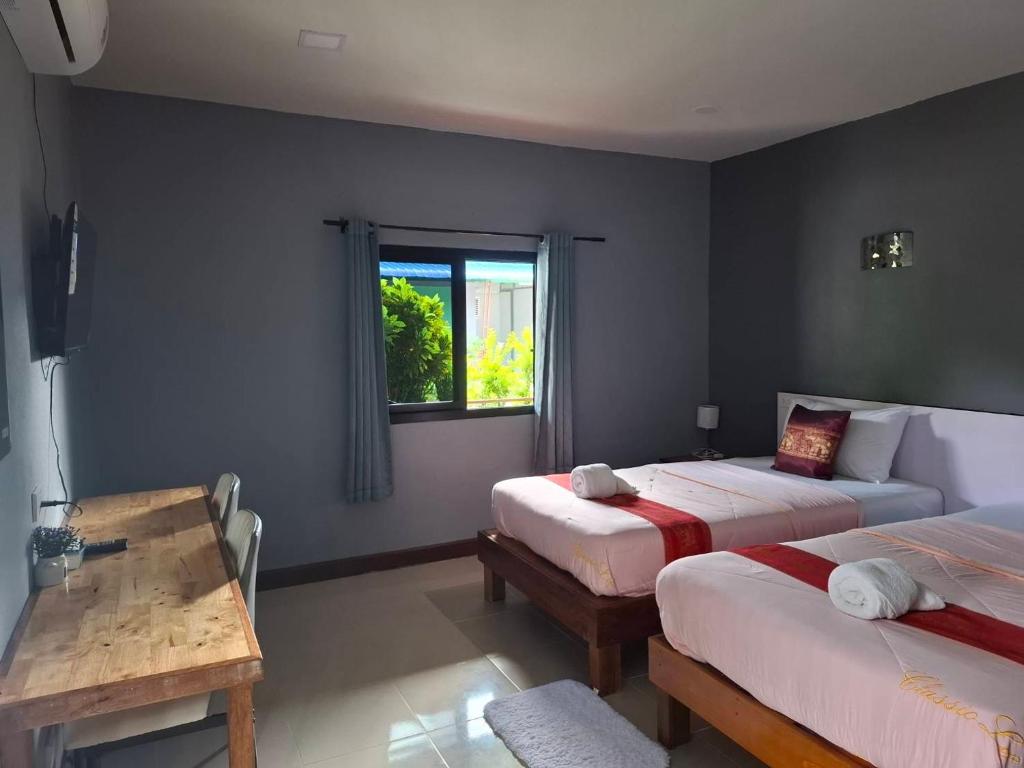 a bedroom with two beds and a table and a window at ใบตองรีสอร์ท in Ban Thung Kha Chomphu