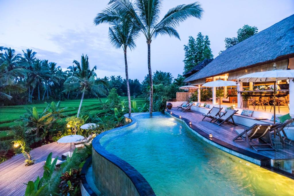 einen Pool mit Stühlen und Sonnenschirmen neben einem Haus in der Unterkunft Calma Ubud Suite & Villas in Ubud