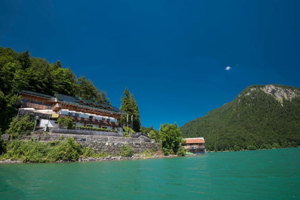 a building on the side of a river with a mountain at Hotel Karwendelblick in Urfeld