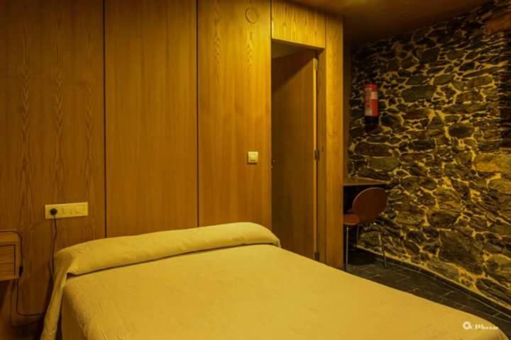 1 dormitorio con cama y pared de piedra en Palloza Baltasar, en Castelo