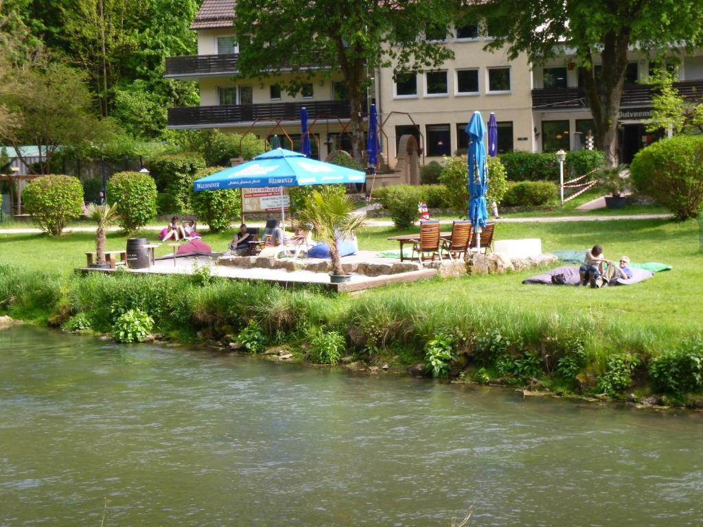 a group of people sitting under an umbrella next to a river at Pension Pulvermühle in Waischenfeld
