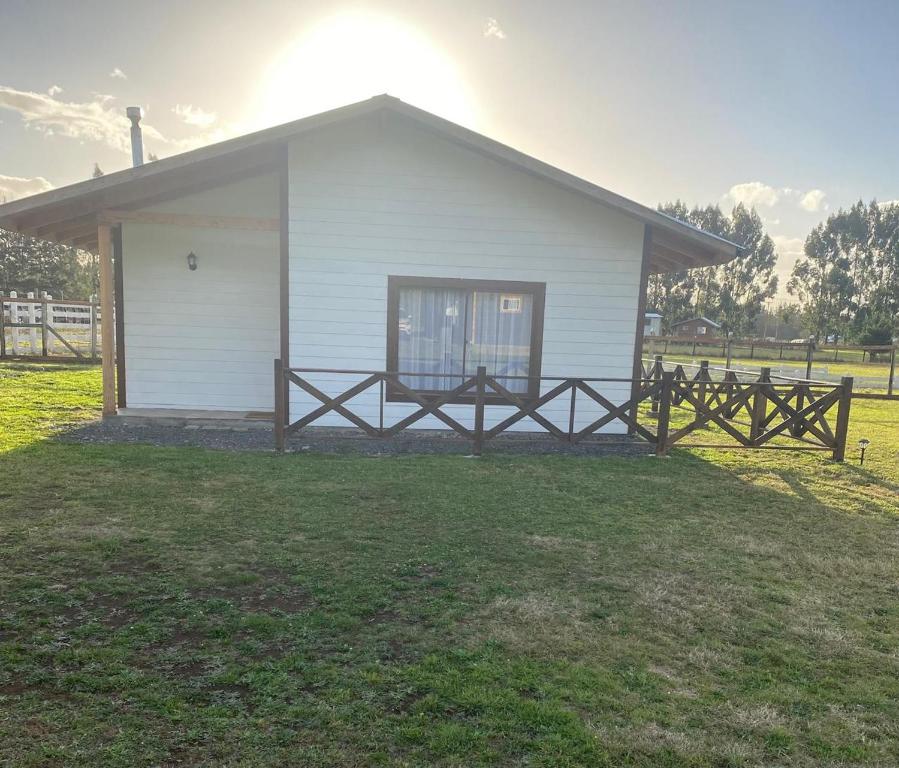 a small white house with a fence in a field at Cabaña Paihuen in Puerto Octay