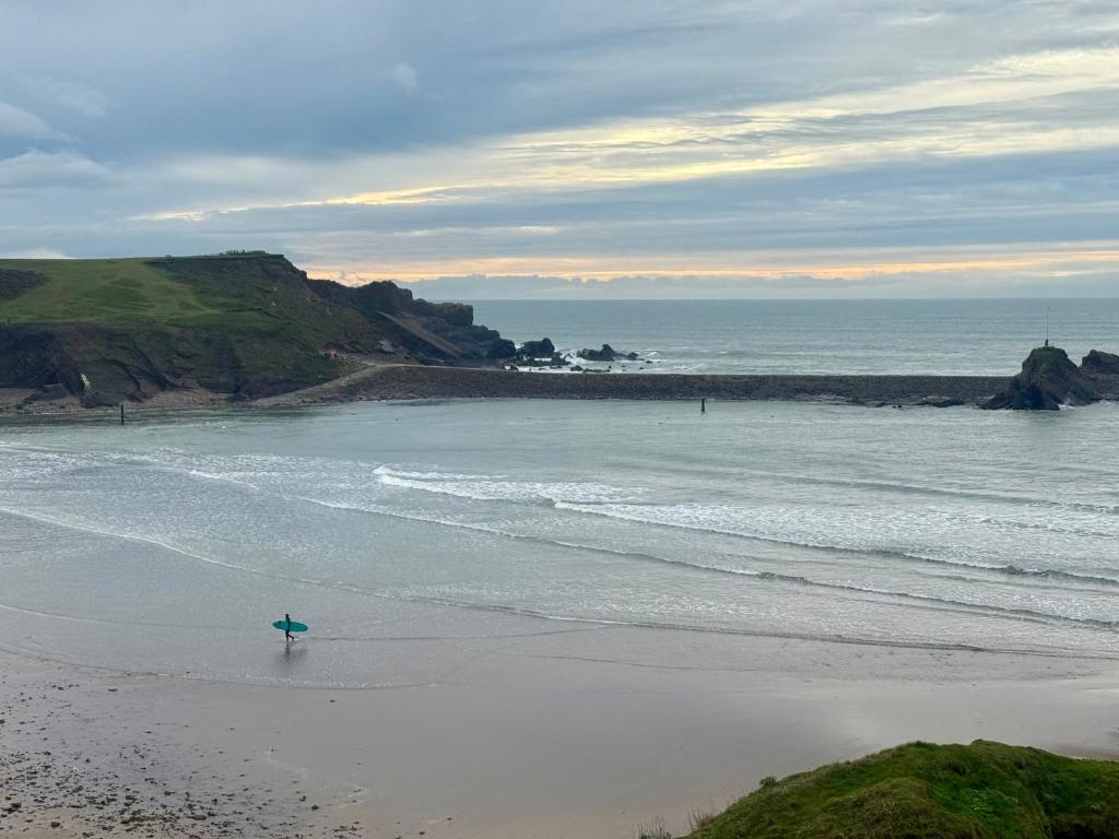 a person standing on a beach with a surfboard at Cornish coastal escape in Bude in Bude