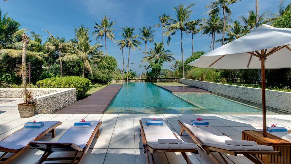 a swimming pool with lounge chairs and an umbrella at Villa Samadhana in Ketewel