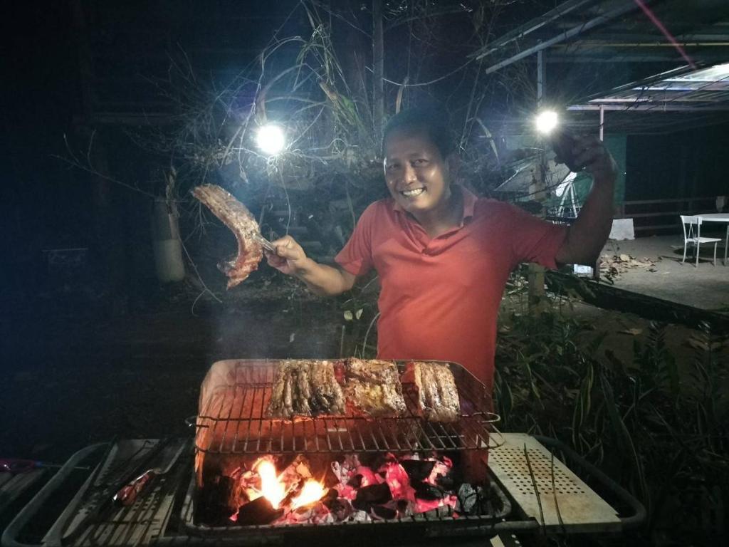 a man standing next to a grill with meat at ดงสัก สไตล์ป่า ไทรโยคน้อย in Ban Phu Pla Kang