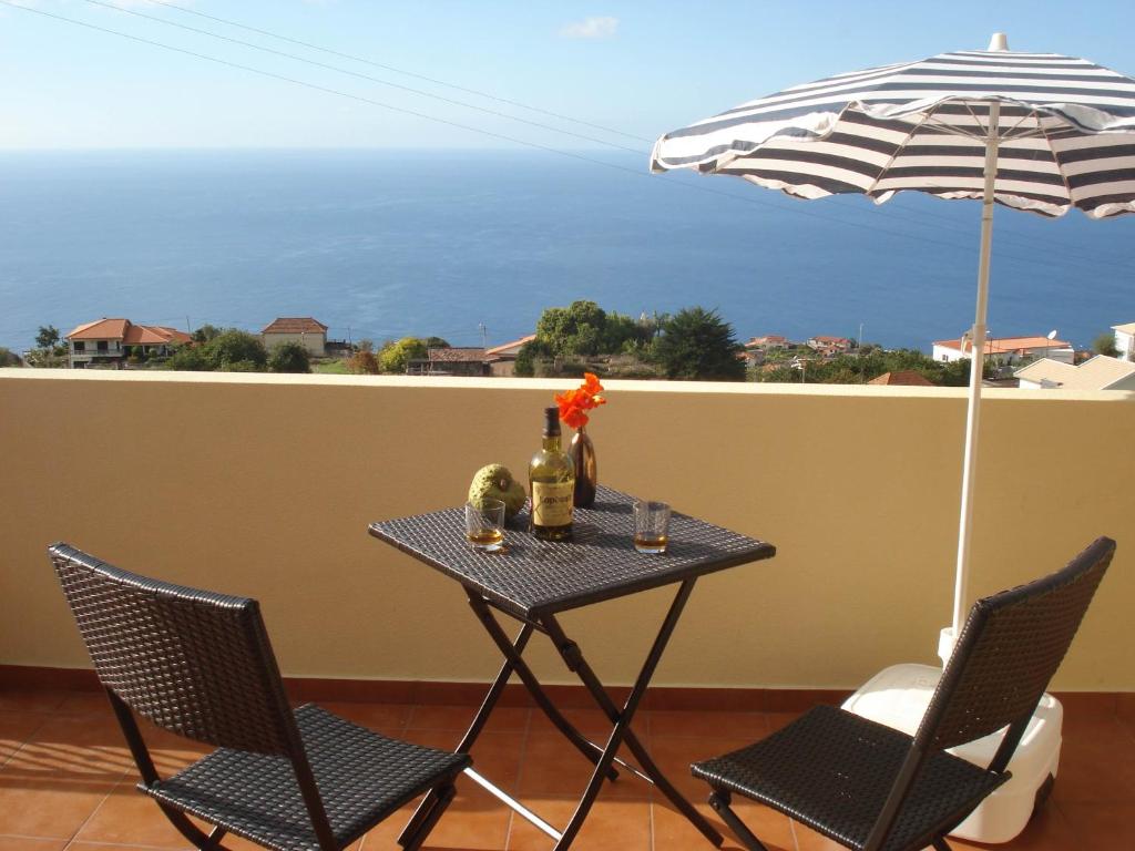 uma mesa com duas cadeiras e um guarda-sol numa varanda em Vista Romantica Madeira em Arco da Calheta