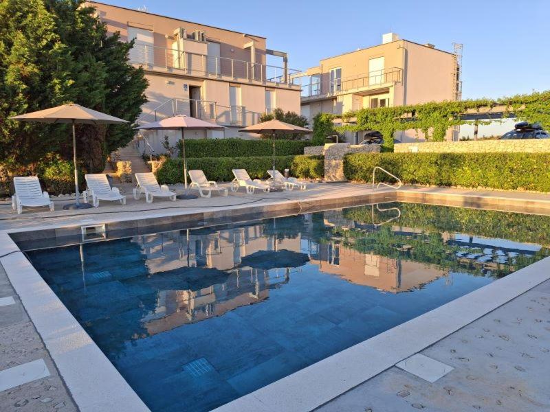 a swimming pool with chairs and umbrellas next to a building at Bella Vista Blu apartman s pogledom na more, Povljana, otok Pag in Povljana