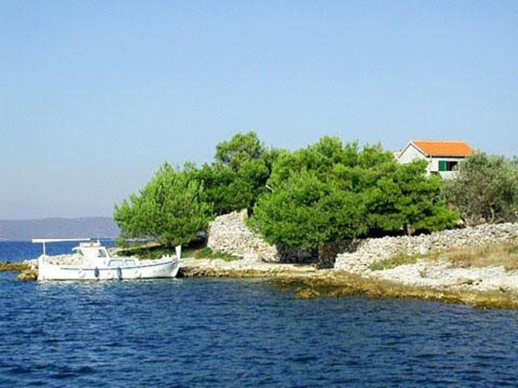a boat sitting in the water next to a house at House Kornati Robinzon in Sit