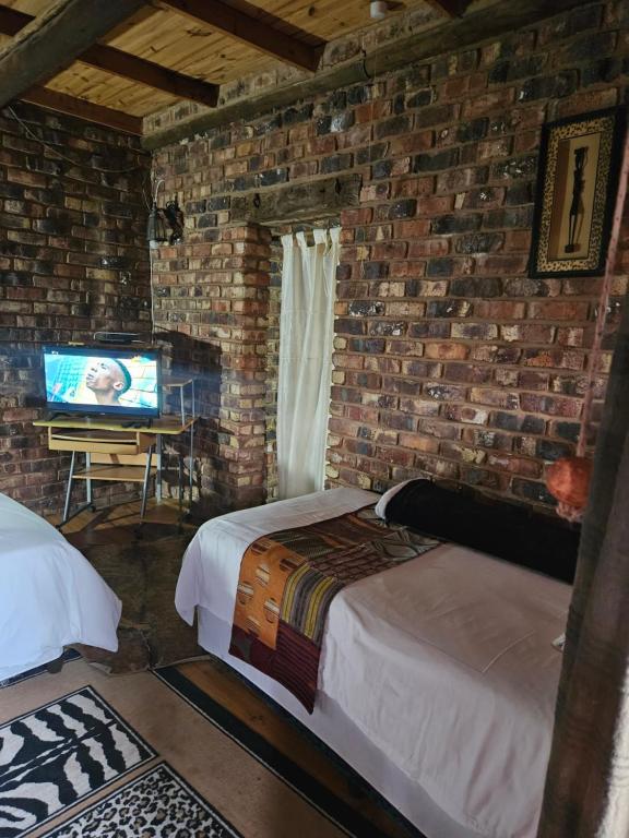 a bedroom with a brick wall with a bed and a television at Die Kliphuisie Gastehuis in Vryburg