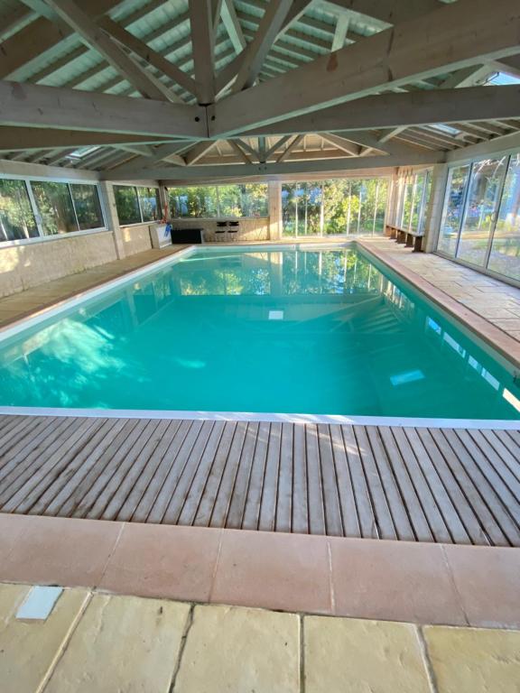 a large swimming pool with a wooden deck and an open ceiling at Le Colombier d'Antan in Les Vans