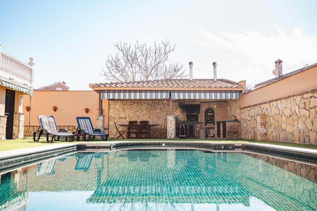 a swimming pool with two chairs and a table at Villa Oropéndola para familias, a pocos minutos de Granada, Piscina agua salada, Parking privado, Barbacoa, Chimenea, 14 pax in Belicena