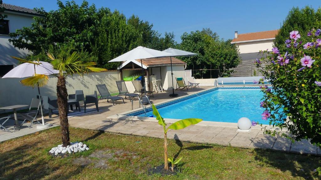 a swimming pool with chairs and an umbrella in a yard at Studio chez Nathalie & Eric in Mérignac