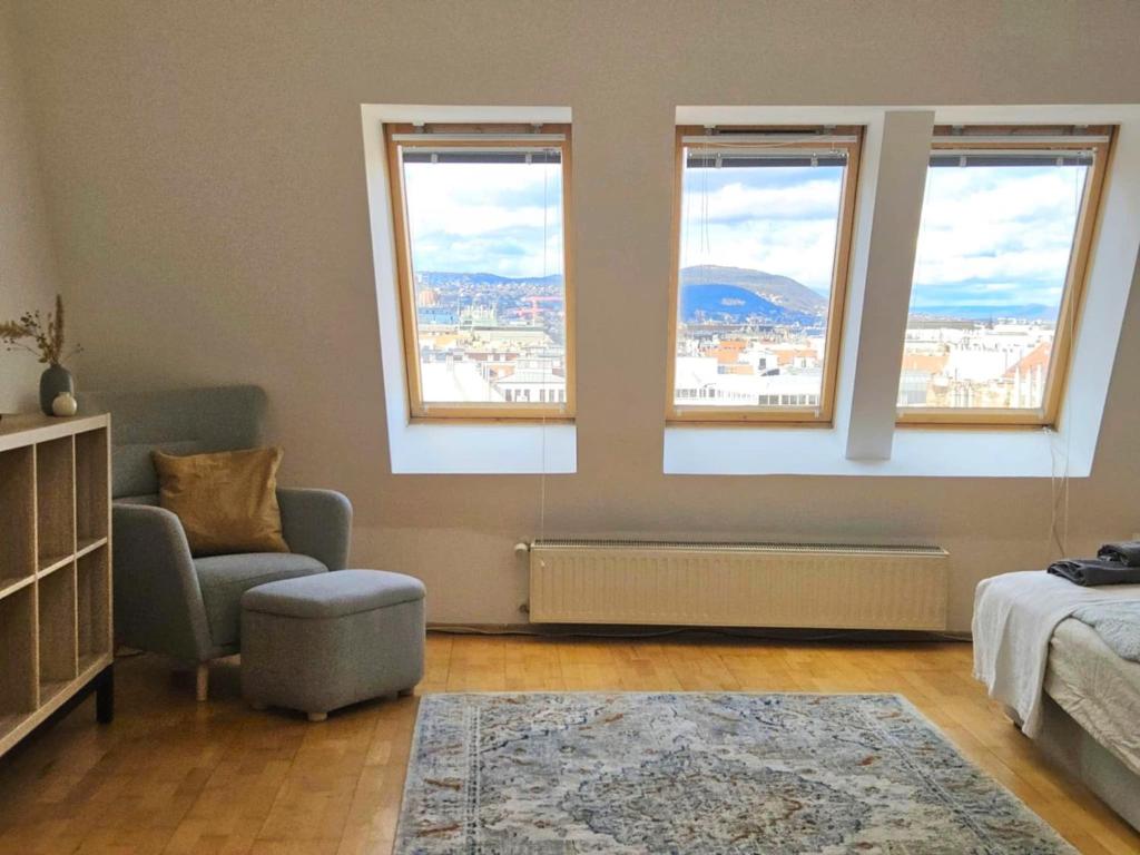 a bedroom with three windows and a bed and a chair at Gellerico Apartments Wesselényi Street in Budapest