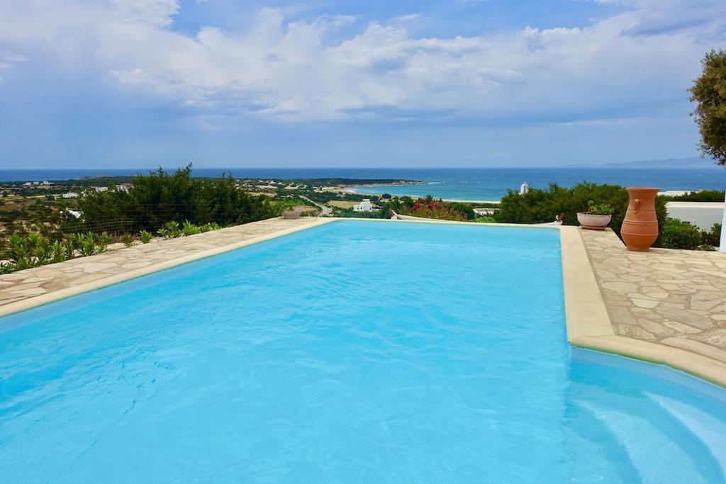 a large blue swimming pool with a view of the ocean at Villa E - Kamari Village in Kastraki
