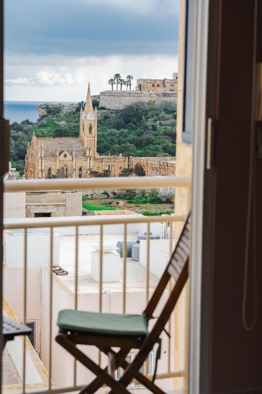 a chair on a balcony with a view of a church at Il-Kannizzata luxurious Gozo penthouse with sea view & pool in Għajnsielem