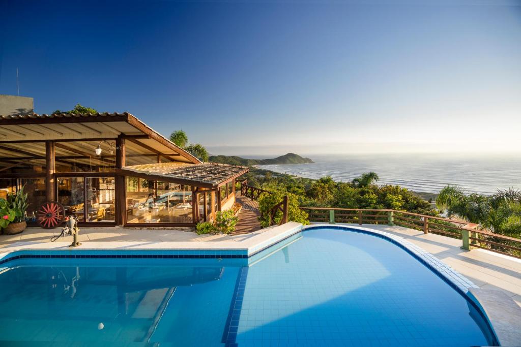 uma piscina em frente a uma casa com o oceano em Pousada Caminho do Rei na Praia do Rosa