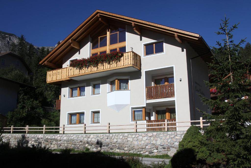 ein weißes Gebäude mit einem Balkon an einer Steinmauer in der Unterkunft Ciasa Rudiferia Appartamenti in Alta Badia in Abtei