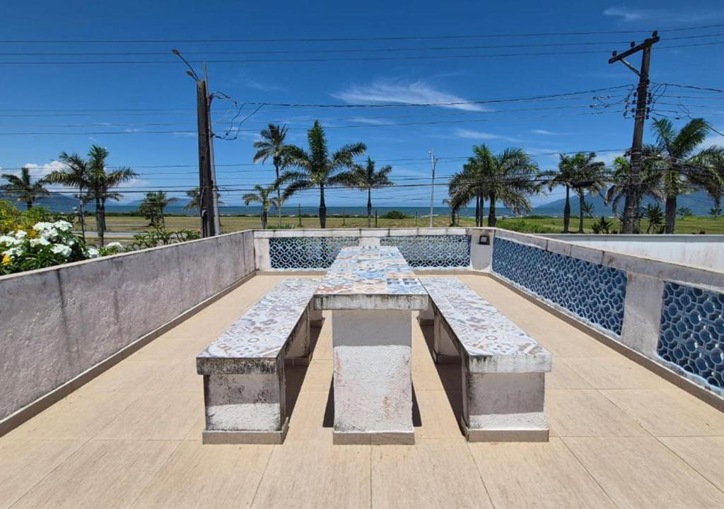 a bench on a wall with palm trees and the ocean at Aloogar Caragua Beach in Caraguatatuba