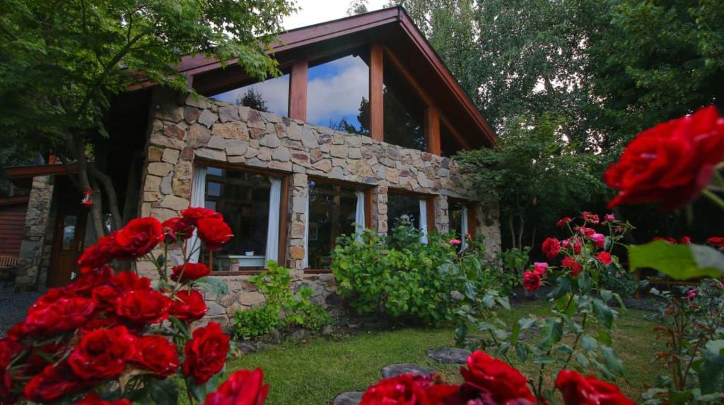 a stone house with red flowers in front of it at Hostería Brisas del Cerro in Villa La Angostura
