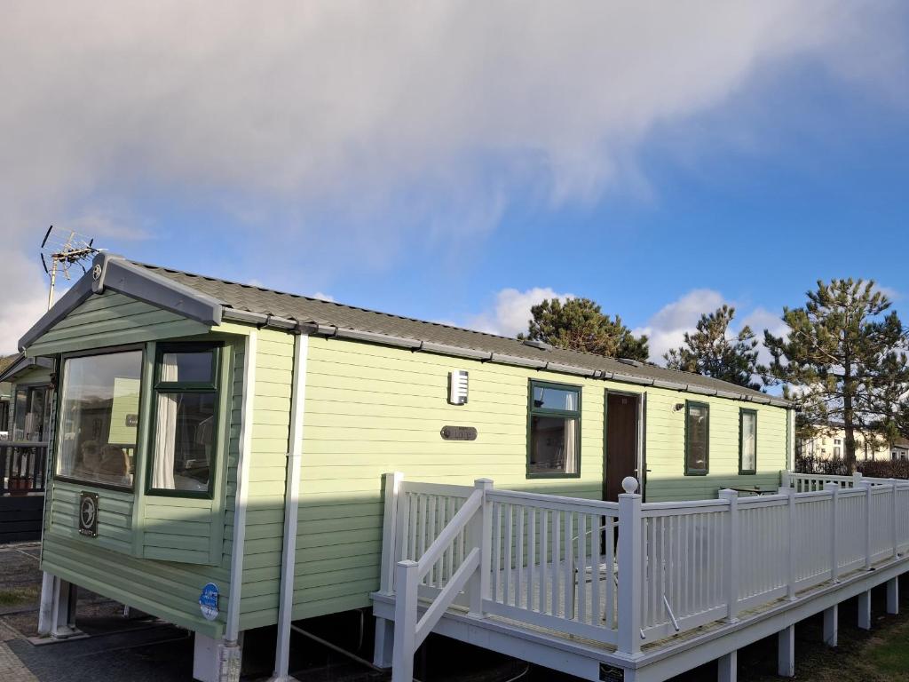 a green and yellow tiny house with a white fence at Glasyln 37 in Porthmadog