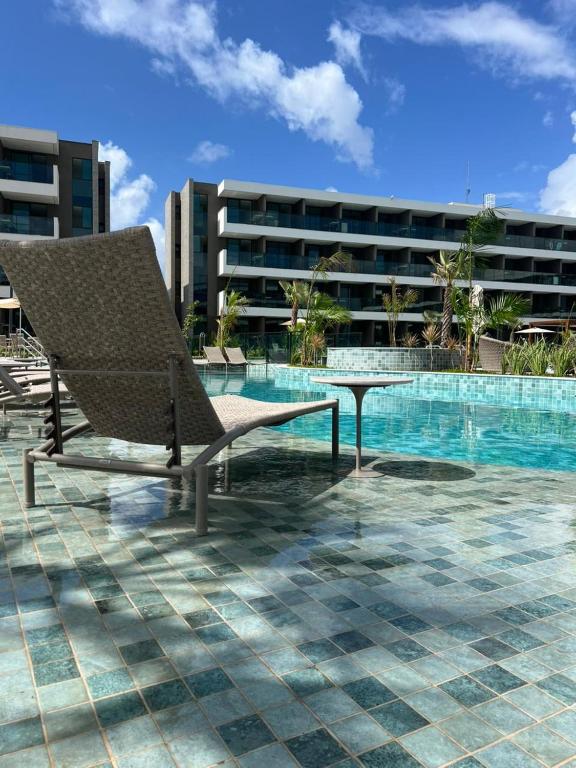 a chair and a table next to a swimming pool at Novíssimo Flat Beach Class Solare - Muro Alto -Soft Open in Porto De Galinhas