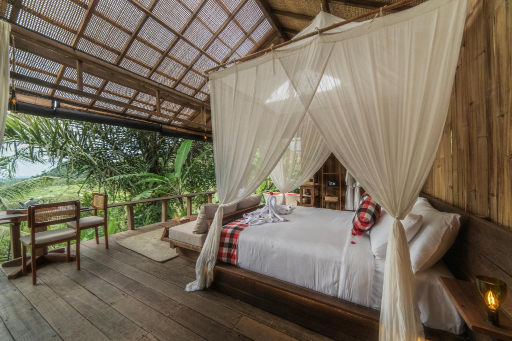 a bedroom with a canopy bed and a table at LeLangit Eco Cabin in Sidemen
