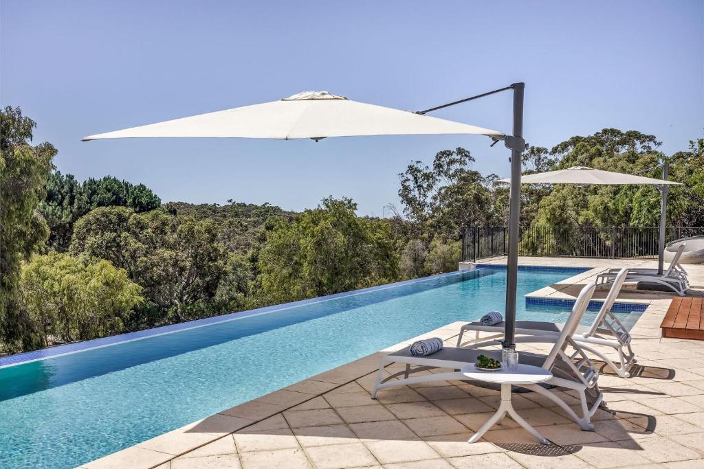 a swimming pool with two chairs and an umbrella at Meelup Vista in Dunsborough