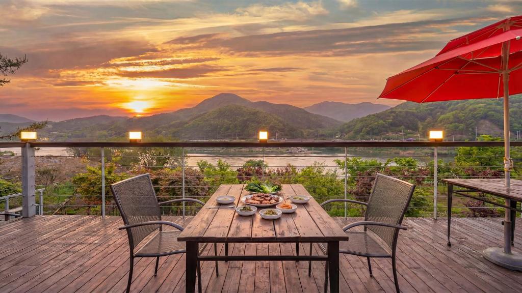 a wooden table and chairs on a deck with a sunset at Gapyeong Rowa River view Pension in Gapyeong